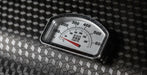 A close-up of a vintage-style temperature gauge with Fahrenheit and Celsius scales, resting on a textured black diamond-patterned surface.