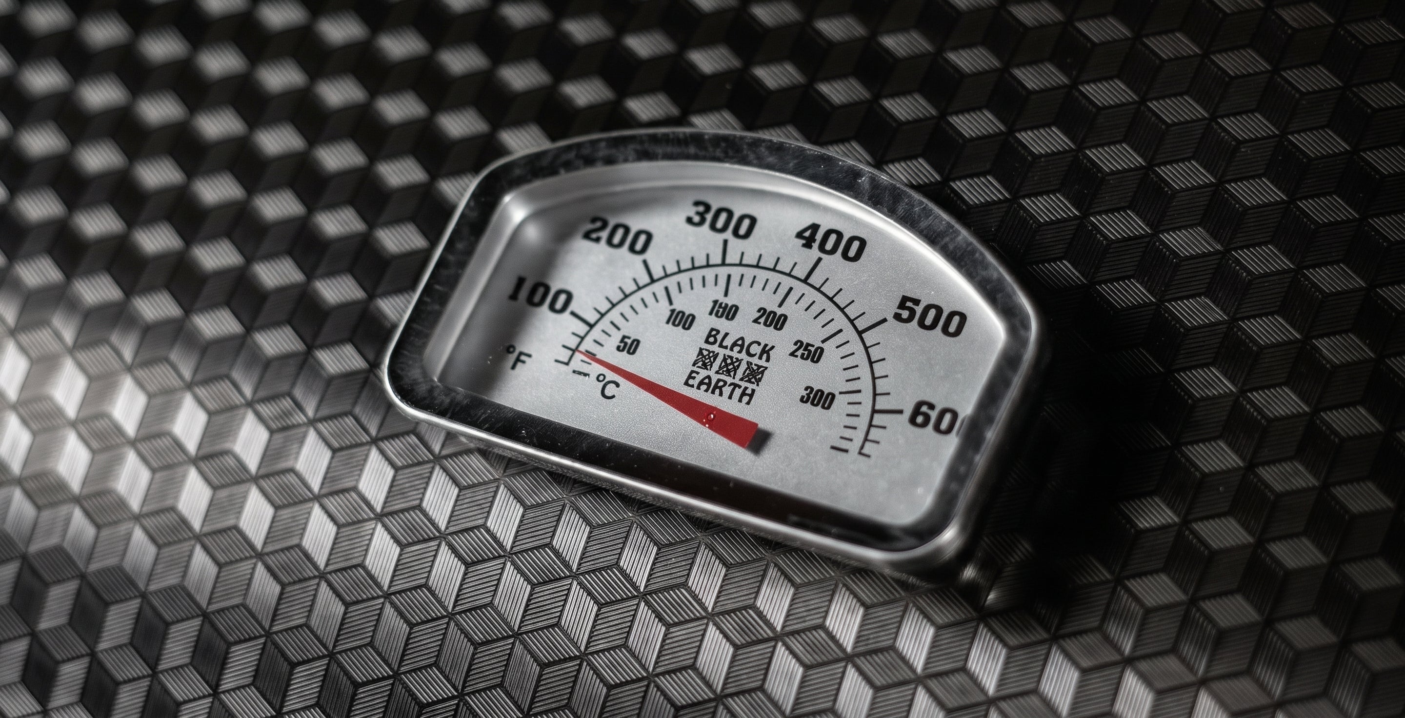 A close-up of a vintage-style temperature gauge with Fahrenheit and Celsius scales, resting on a textured black diamond-patterned surface.