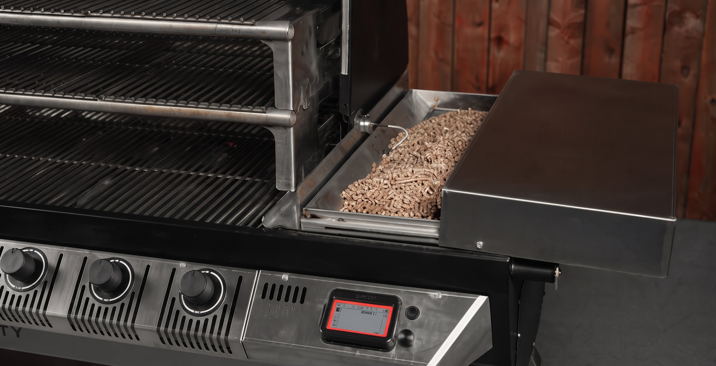 A stainless steel gas grill with a side tray holding wood chips, shown against a dark wood plank background.