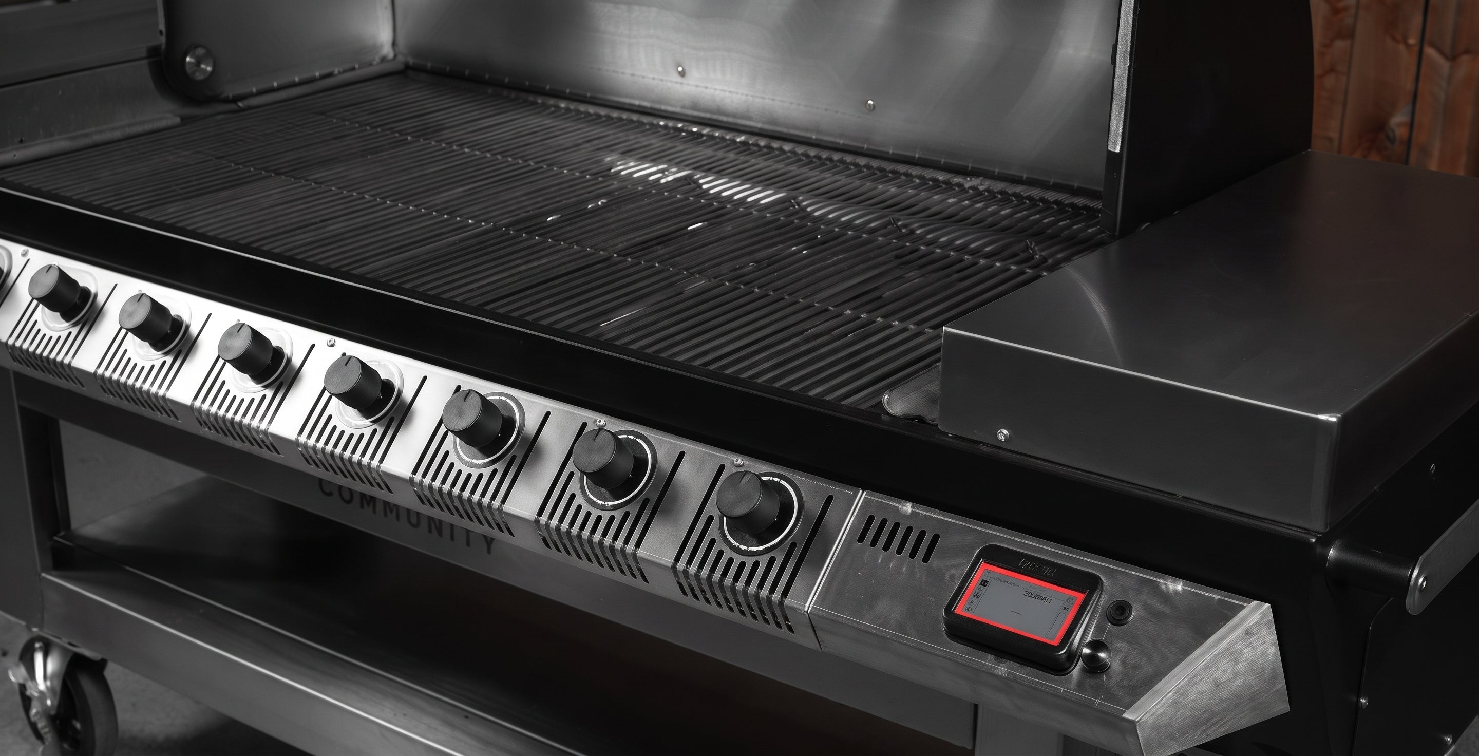 Close-up of a black and stainless steel gas grill showing the control knobs, grates, side shelf, and a digital temperature display with a red border.