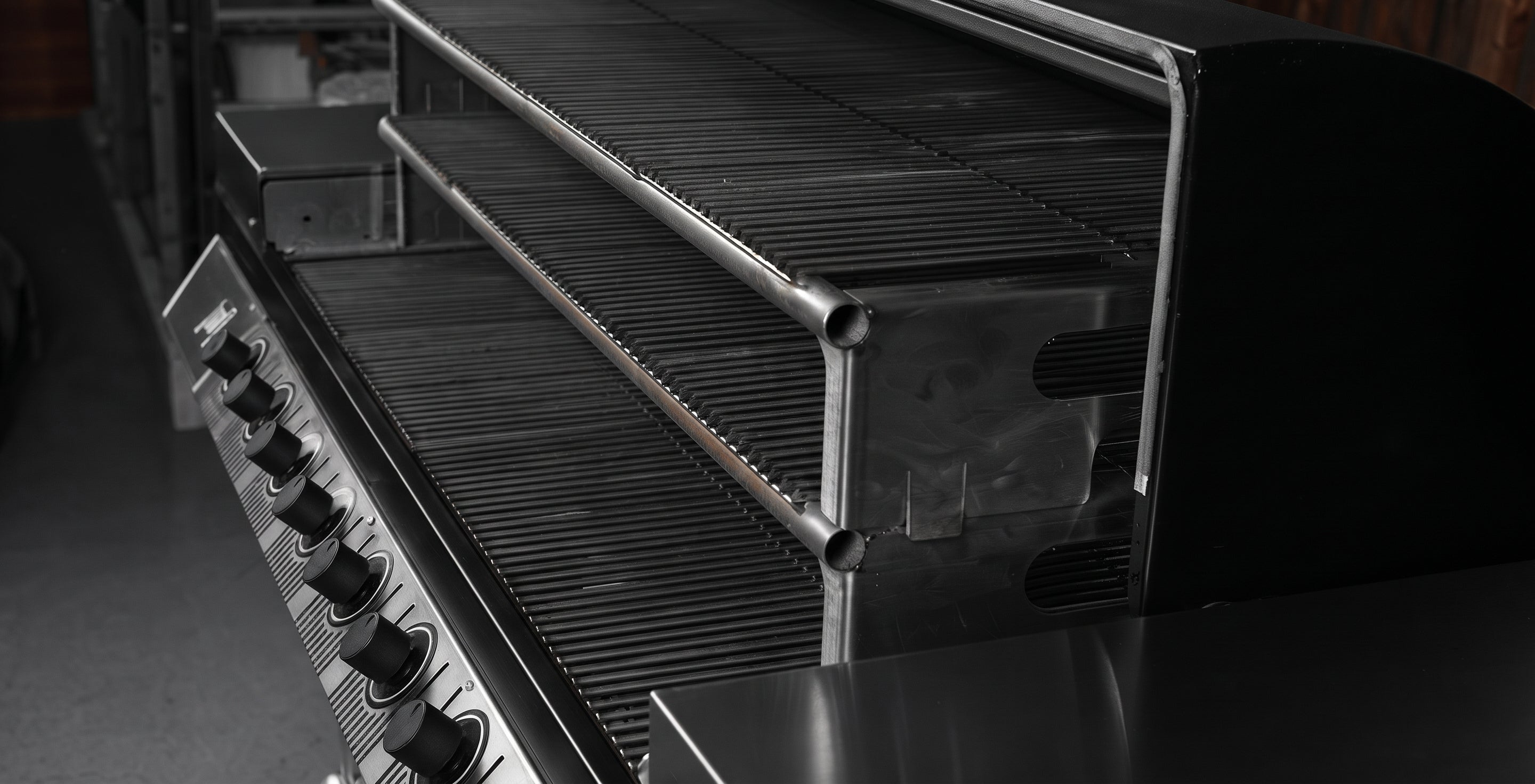 Close-up of a stainless steel gas grill showing the control knobs on the left and the interior grates and firebox chamber.