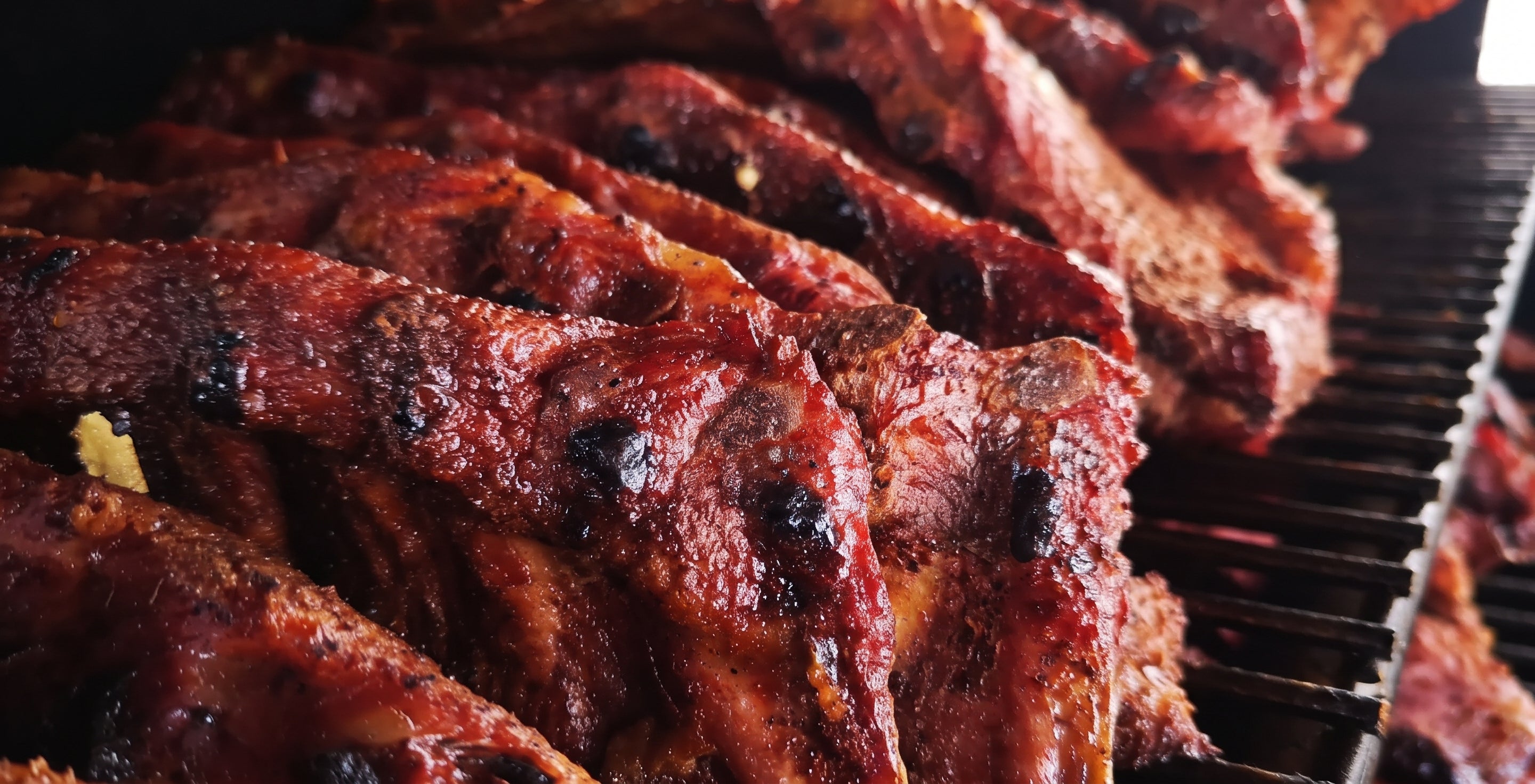 Close-up of glazed barbecue ribs cooking on a grill, with glossy sauce and charred grill marks visible.