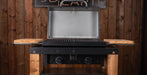 A black gas grill with an open lid and side tables, set against a rustic wooden plank wall.