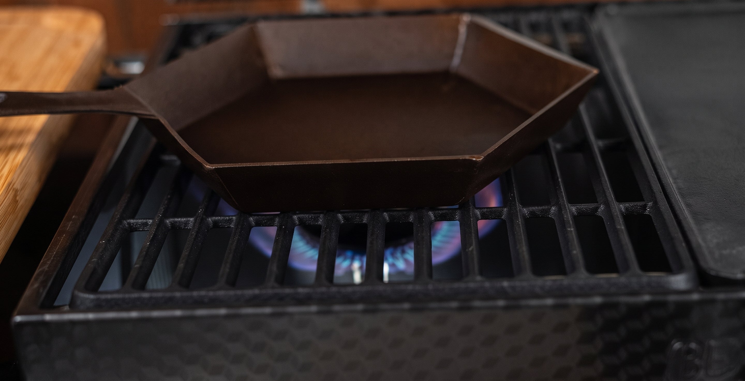 A dark cast iron octagonal pan sits on a gas stove burner with a blue flame visible underneath.