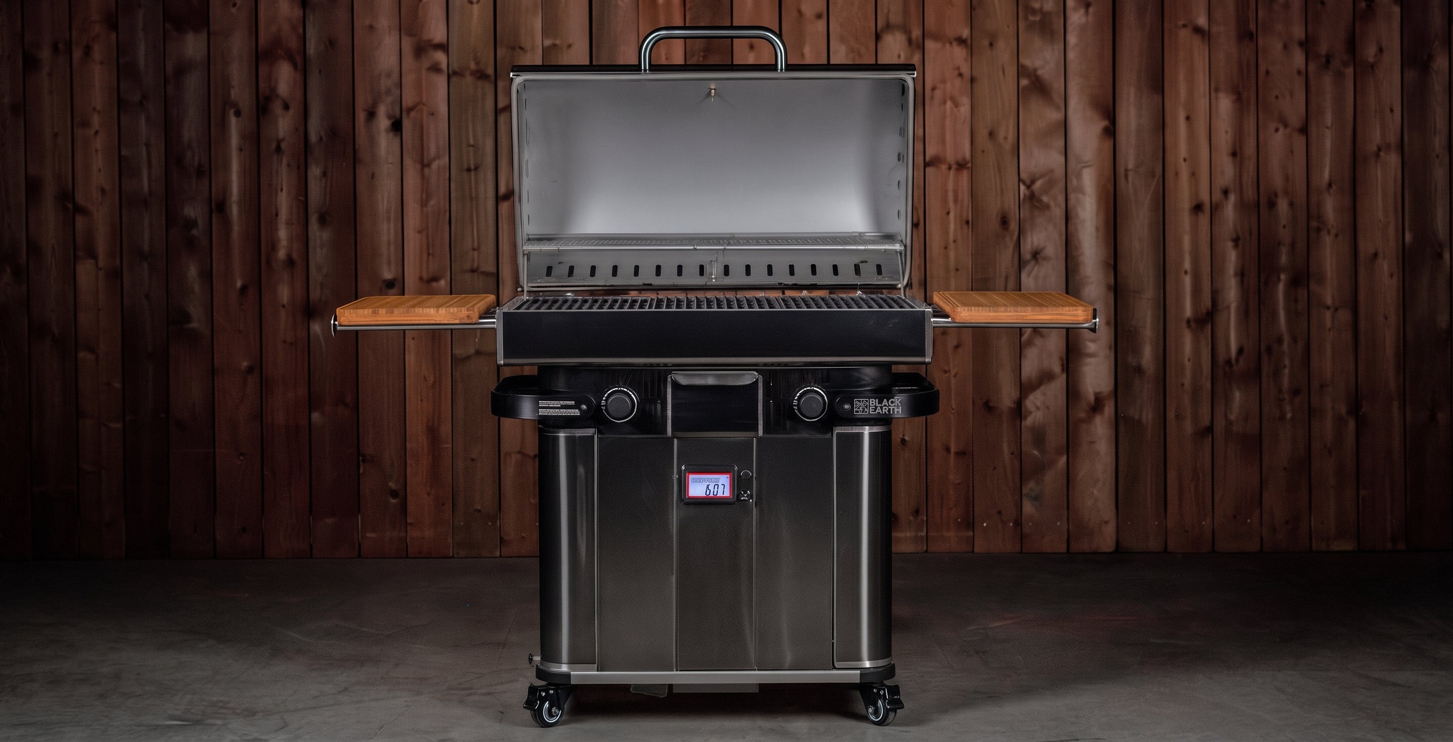 A stainless steel gas grill with side tables and a lid handle, shown open against a dark wood plank wall background.