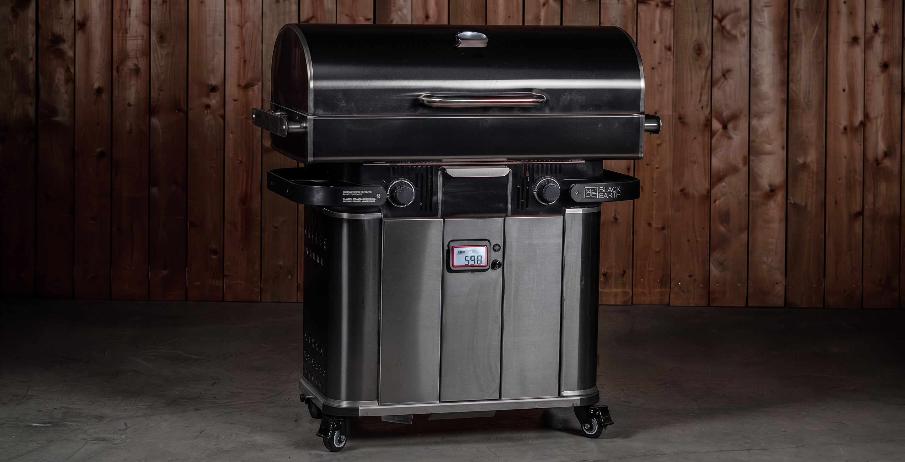 A stainless steel and black gas grill with a lid, side shelves, and caster wheels, positioned in front of a dark wood plank wall.