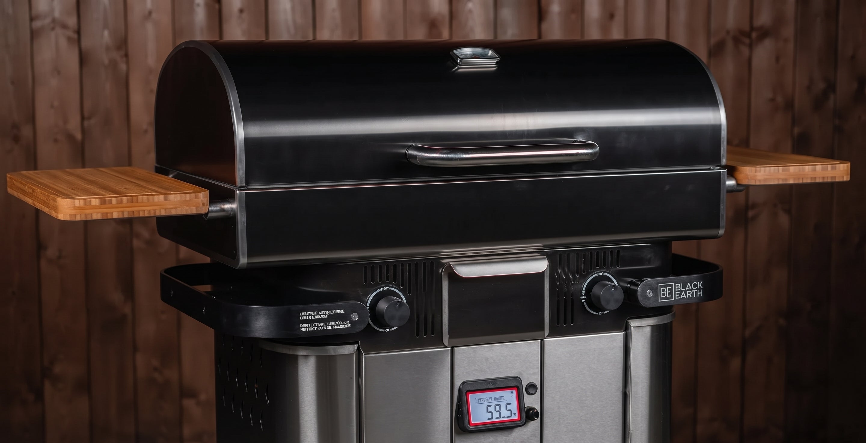 A black and stainless steel outdoor grill with wooden side shelves, set against a dark wood plank wall background.