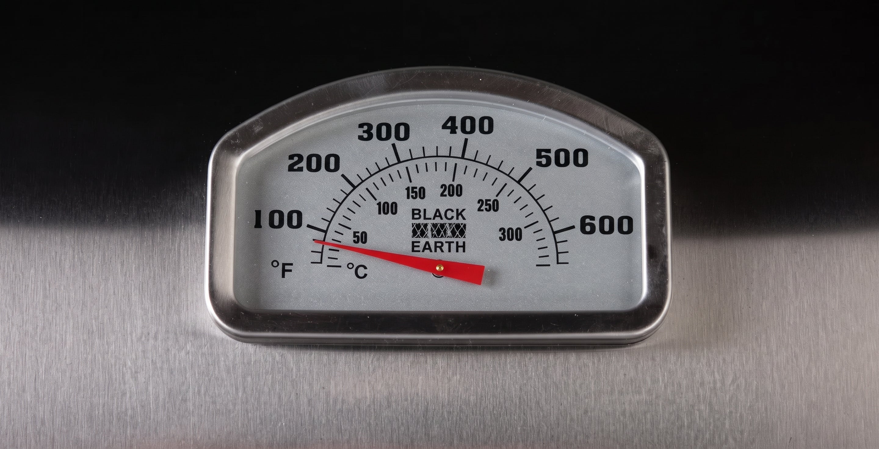 A close-up of a Black Earth thermometer gauge with Fahrenheit and Celsius scales, mounted on a brushed metal surface against a dark background.