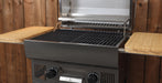 A black gas grill with a stainless steel interior, shown open with wooden side tables attached on both sides, set against a wooden plank wall.