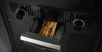Close-up of a black wood-burning stove or fireplace insert with a pull-out door showing stacked wood logs inside, set against a dark textured background.