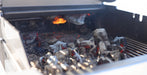 Close-up of a grill with glowing embers and charcoal coals inside the cooking chamber.