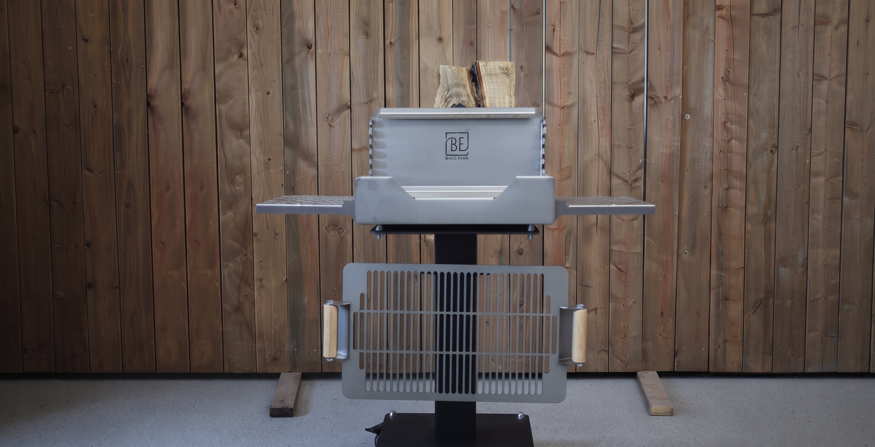A charcoal grill with a gray metal body and black stand, positioned in front of a rustic wood-paneled wall.