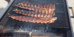 Three racks of grilled ribs cooking on a black charcoal grill with visible smoke and glowing coals below.